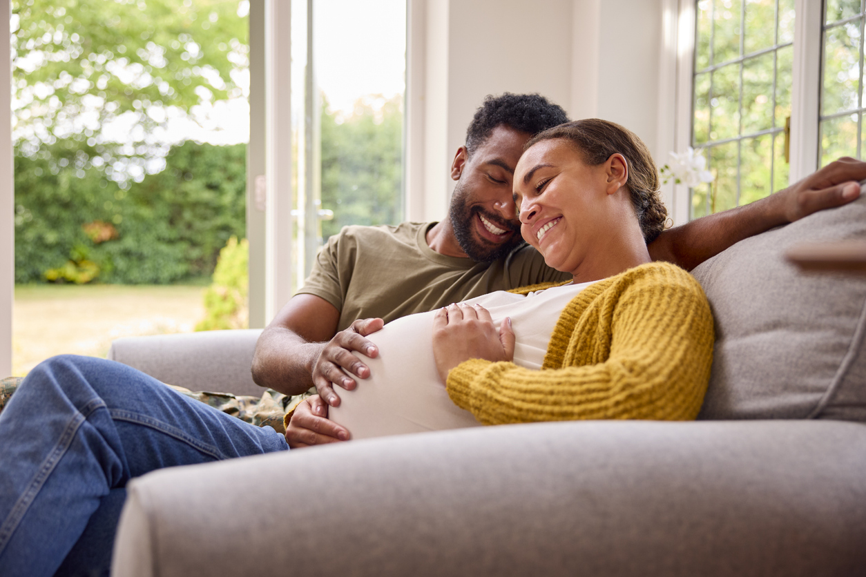 Pregnant Couple With Woman Sitting Next To Army Husband In Uniform Home On Leave